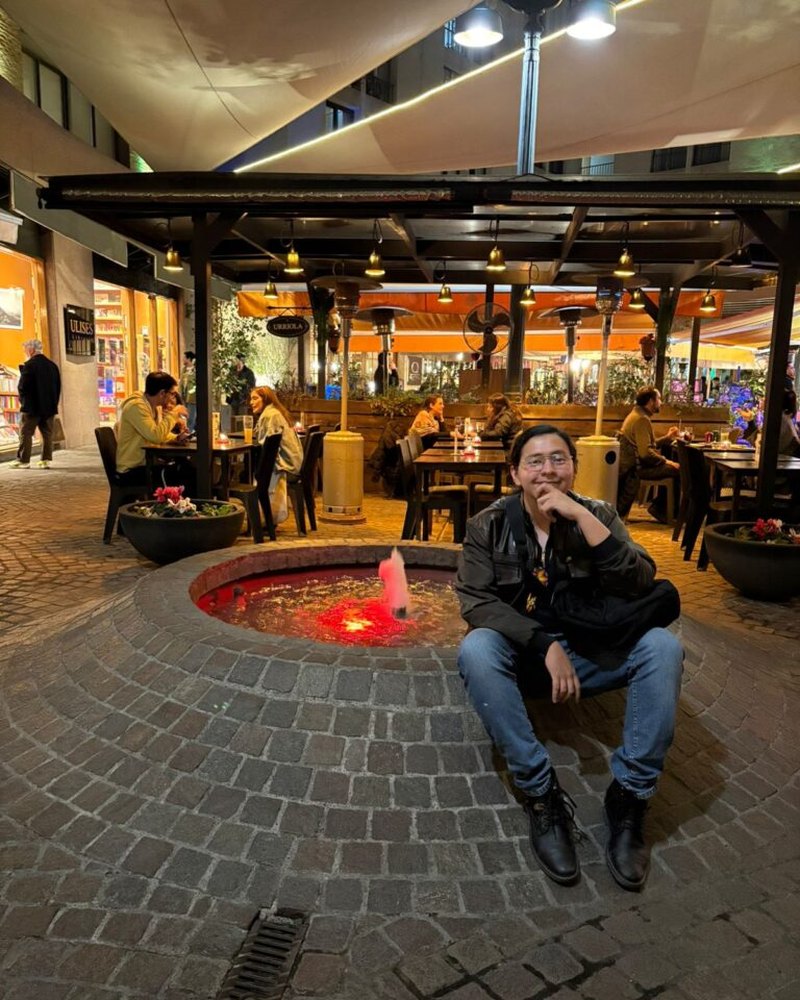 Harby Trujillo assis dans un espace culturel urbain lors d’un moment de conversation et d’observation.